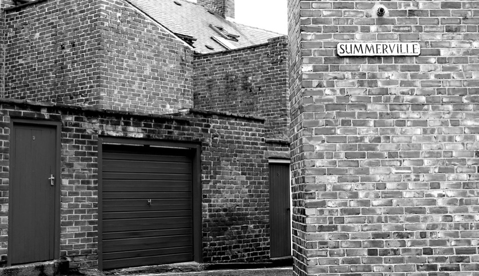A back lane of stone and brick walls with a garage door behind houses in Durham