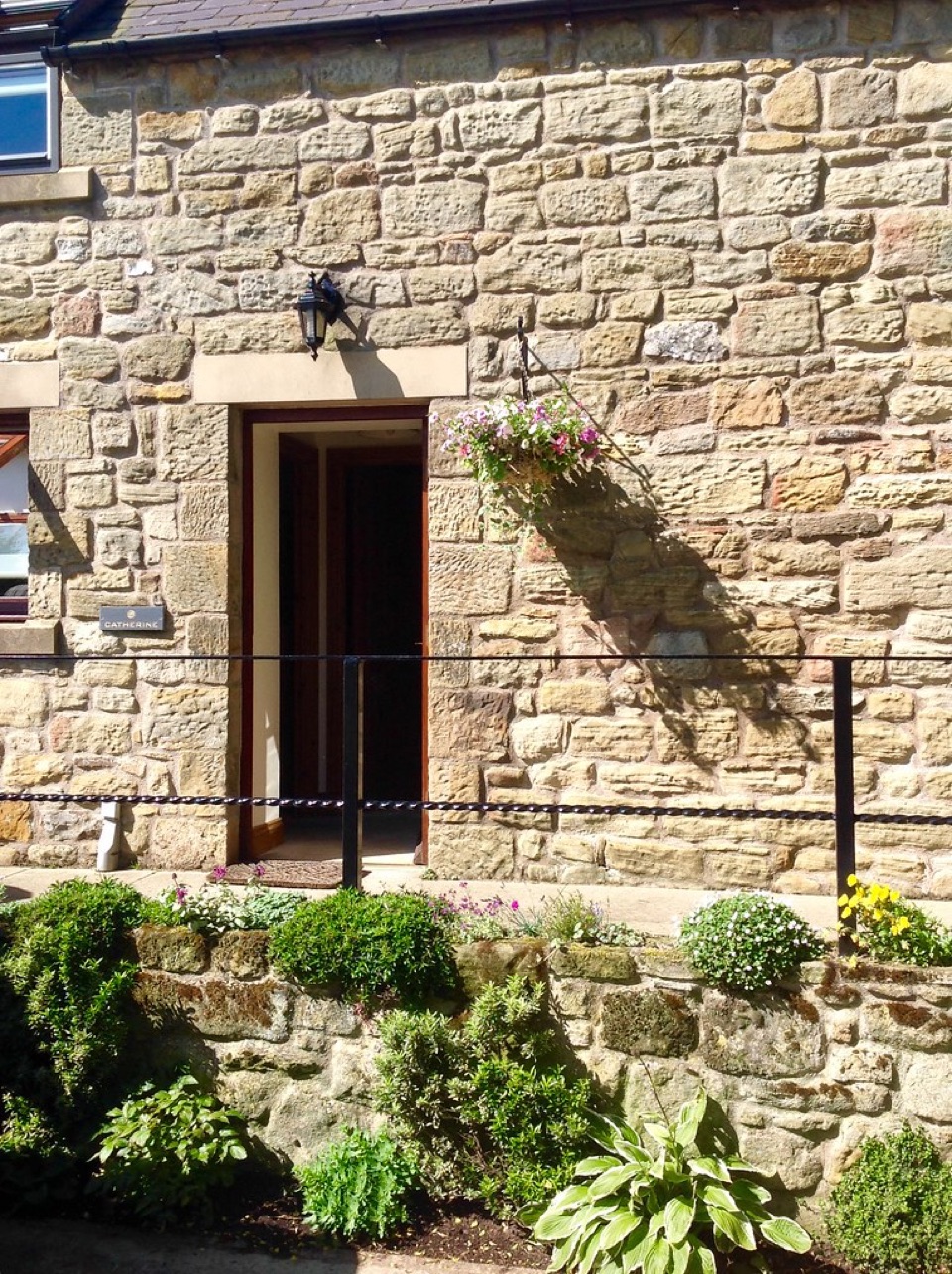 A stone wall with a timber door in it and planting at its foot